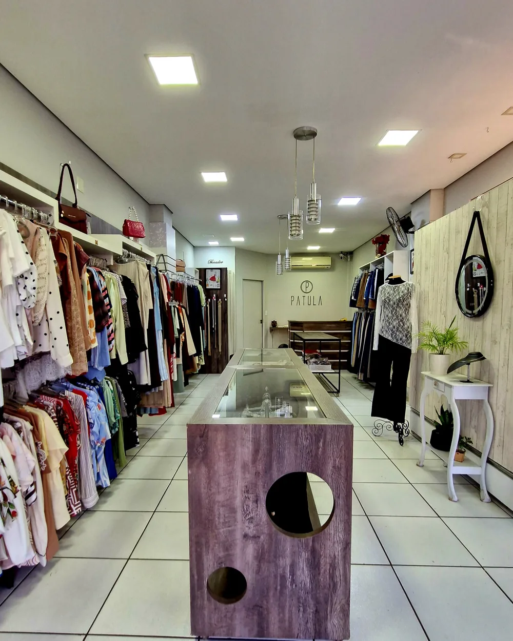 Corredor central e araras de roupas femininas da loja Patula Modas
